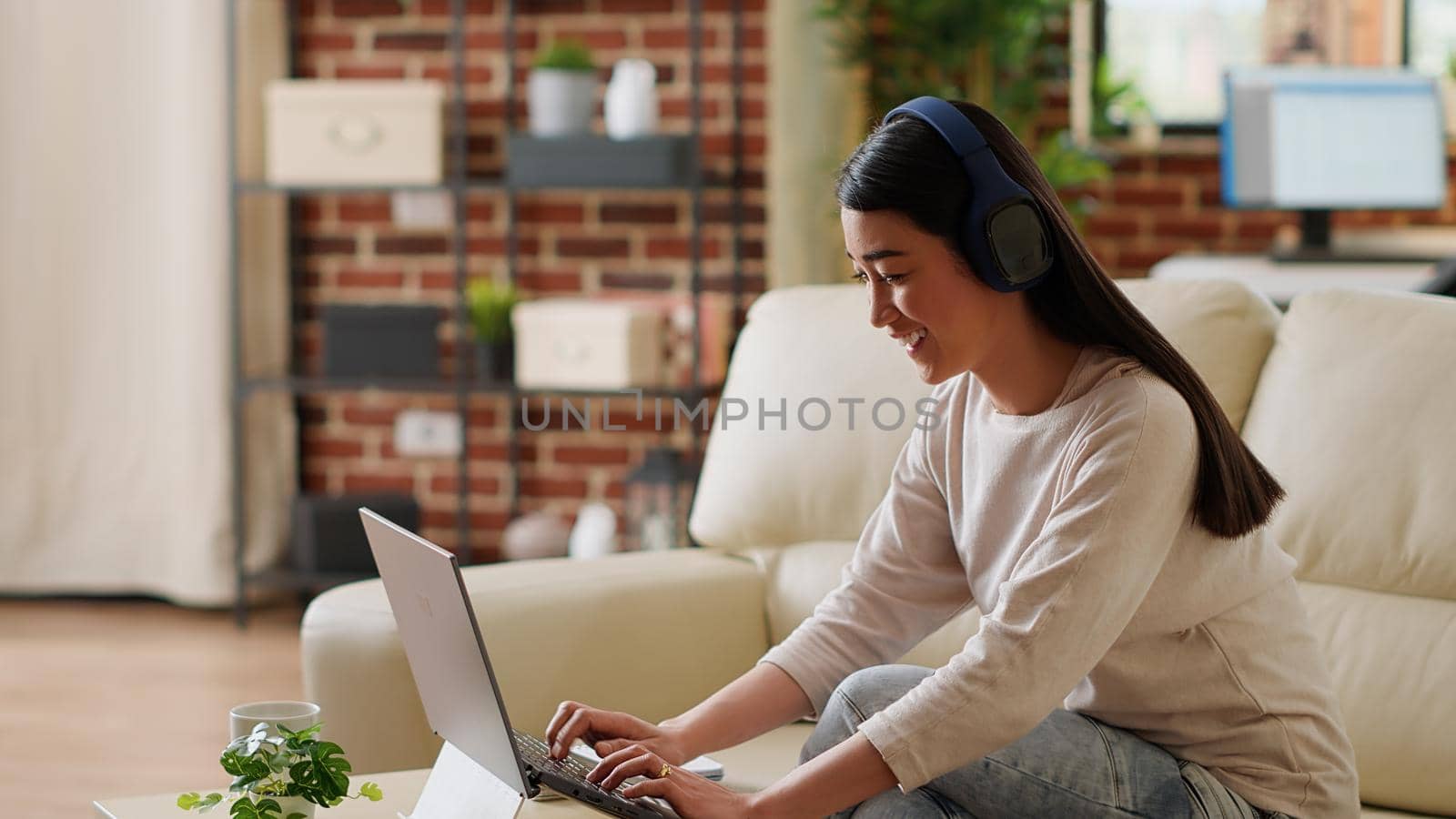Happy woman wearing headphones while listening music and working from home by DCStudio