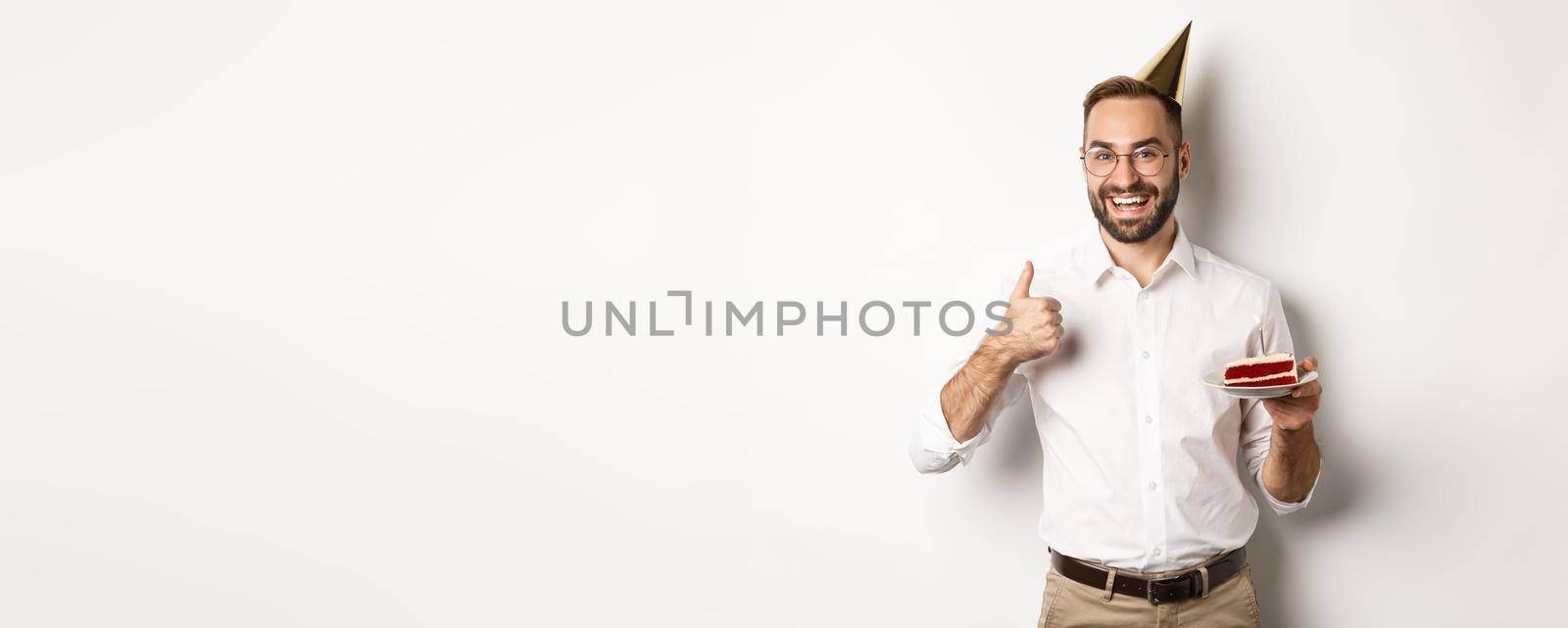 Holidays and celebration. Satisfied man enjoying b-day party, holding birthday cake and showing thumb up in approval, recommending something, white background.