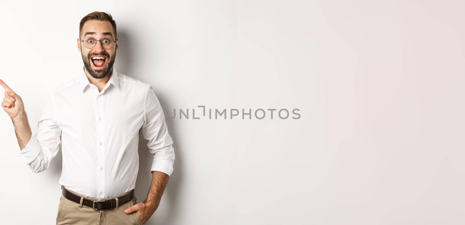 Surprised and excited man making announcement. Businessman pointing finger left at copy space, white background.