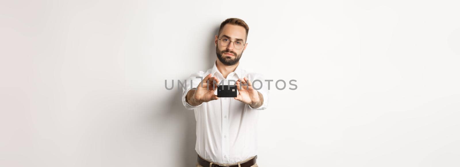 Serious businessman showing credit card, standing over white background by Benzoix