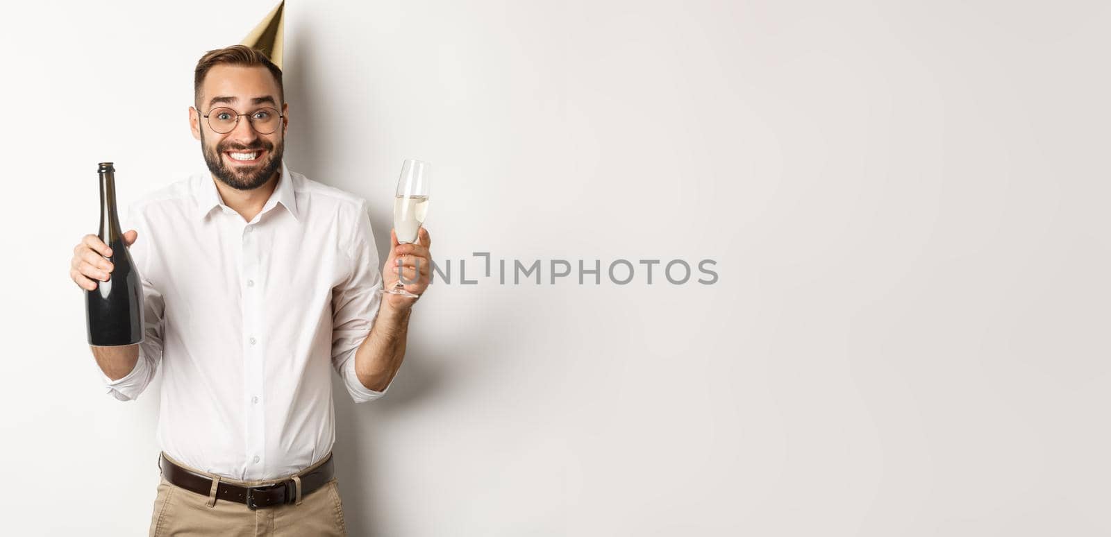 Celebration and holidays. Happy birthday guy enjoying b-day party, wearing funny cone hat and drinking champagne, white background.