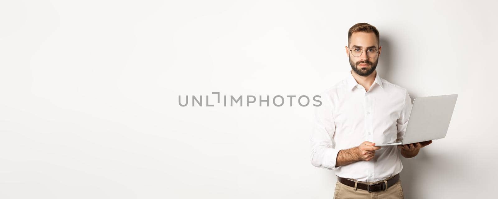 Business. Handsome manager working on laptop, holding computer and looking at camera, standing over white background.