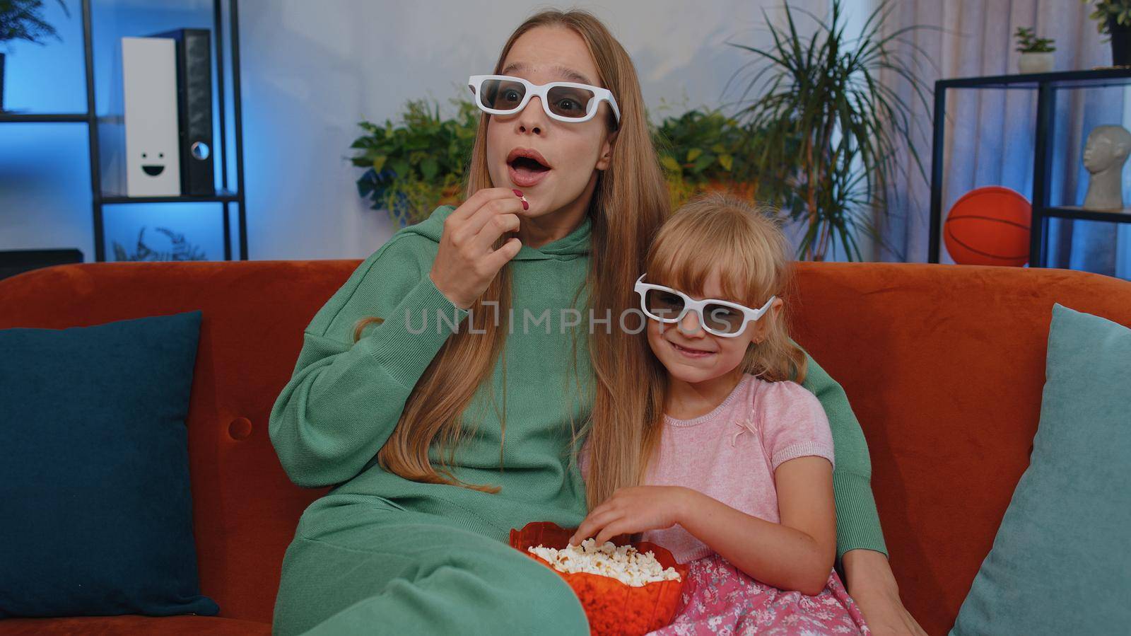 Girls friends siblings watching favorite tv show movie and eating popcorn, sitting on sofa. Female children kids family having fun laughing, relaxing, watch television online stream at home on couch