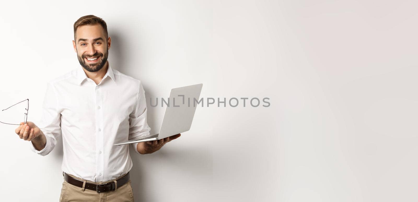 Professional confident businessman doing job on laptop, looking satisfied, standing over white background.