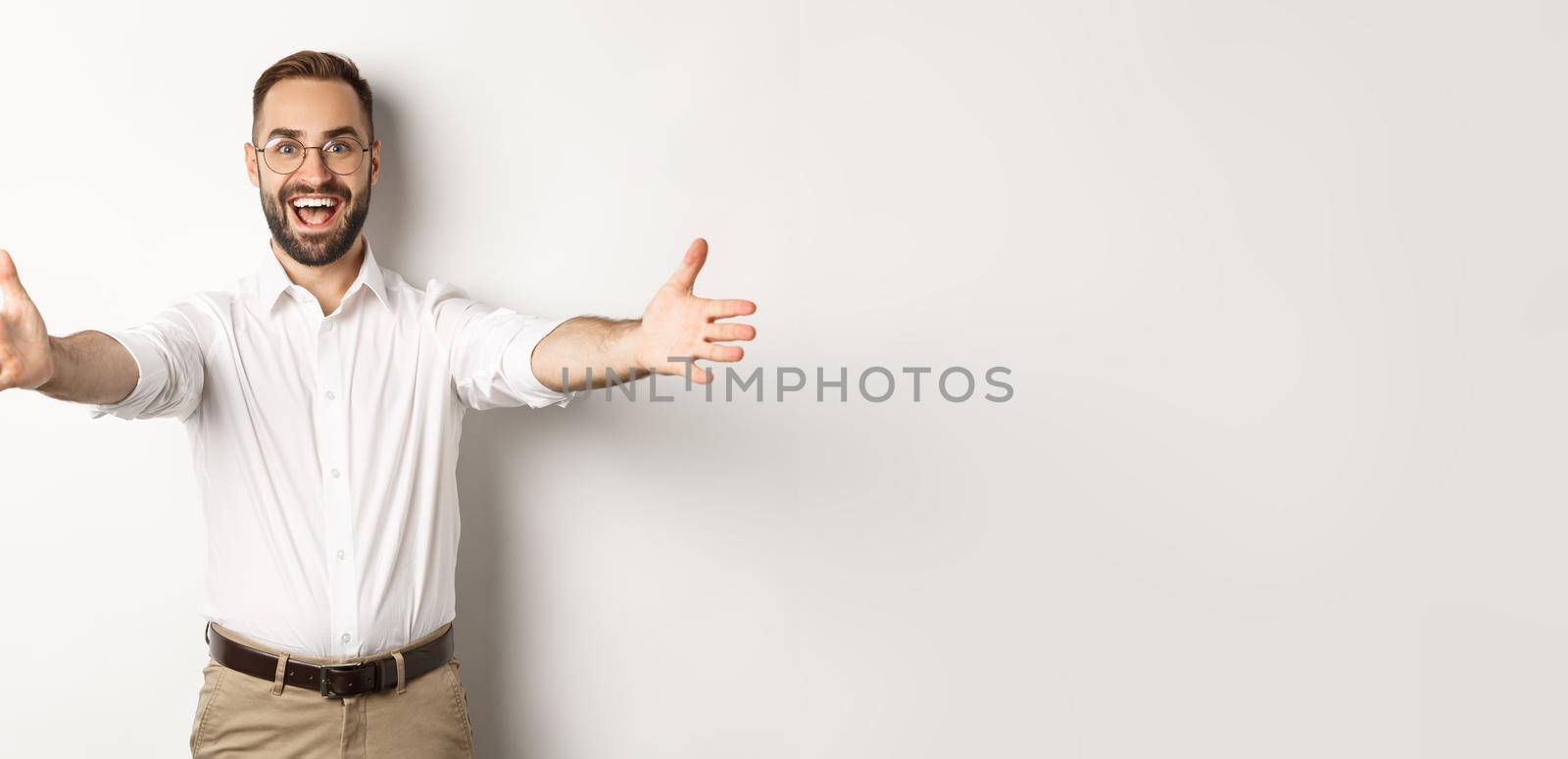 Happy man stretching hands in warm welcome, waiting for hug or greeting someone, standing over white background.
