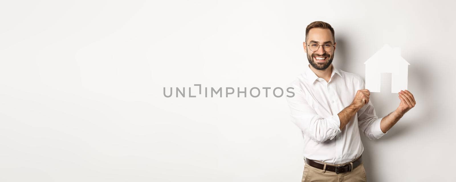Real estate. Handsome man showing house model and smiling, broker showing apartments, standing over white background.