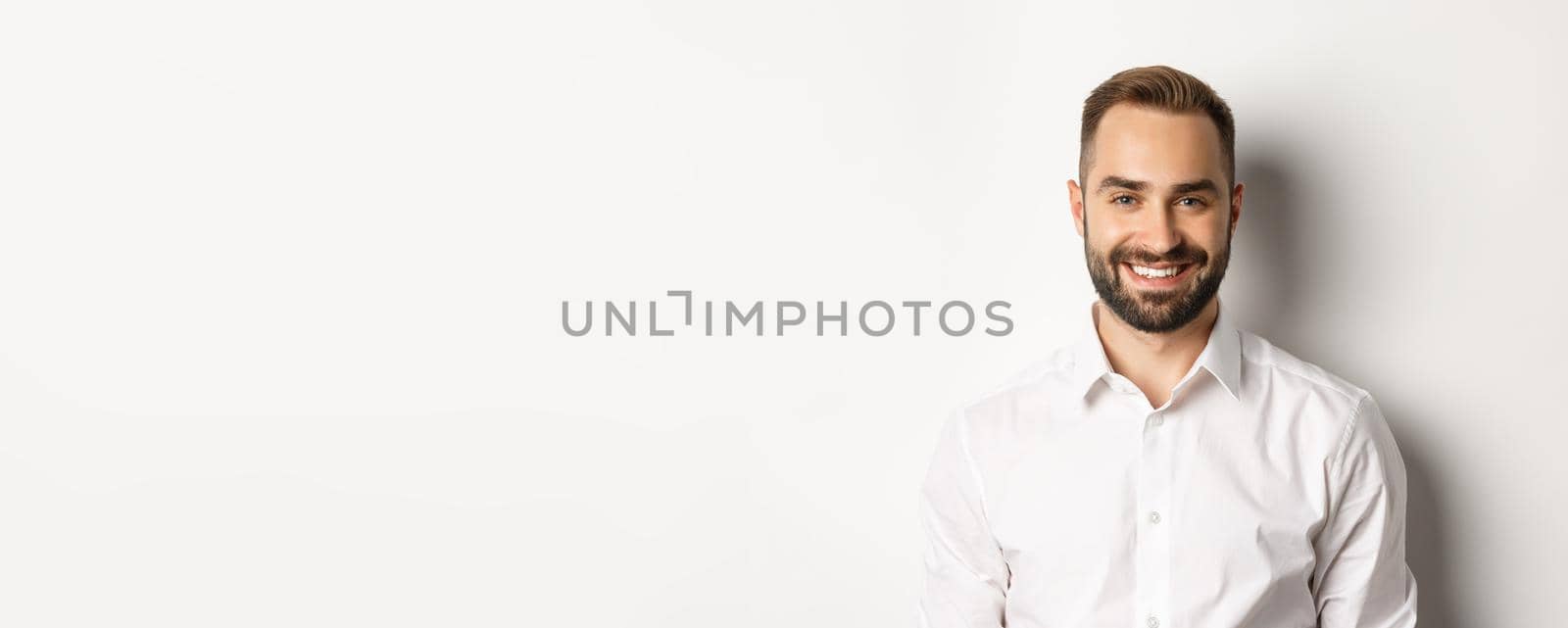 Close-up of confident male employee in white collar shirt smiling at camera, standing self-assured against studio background.