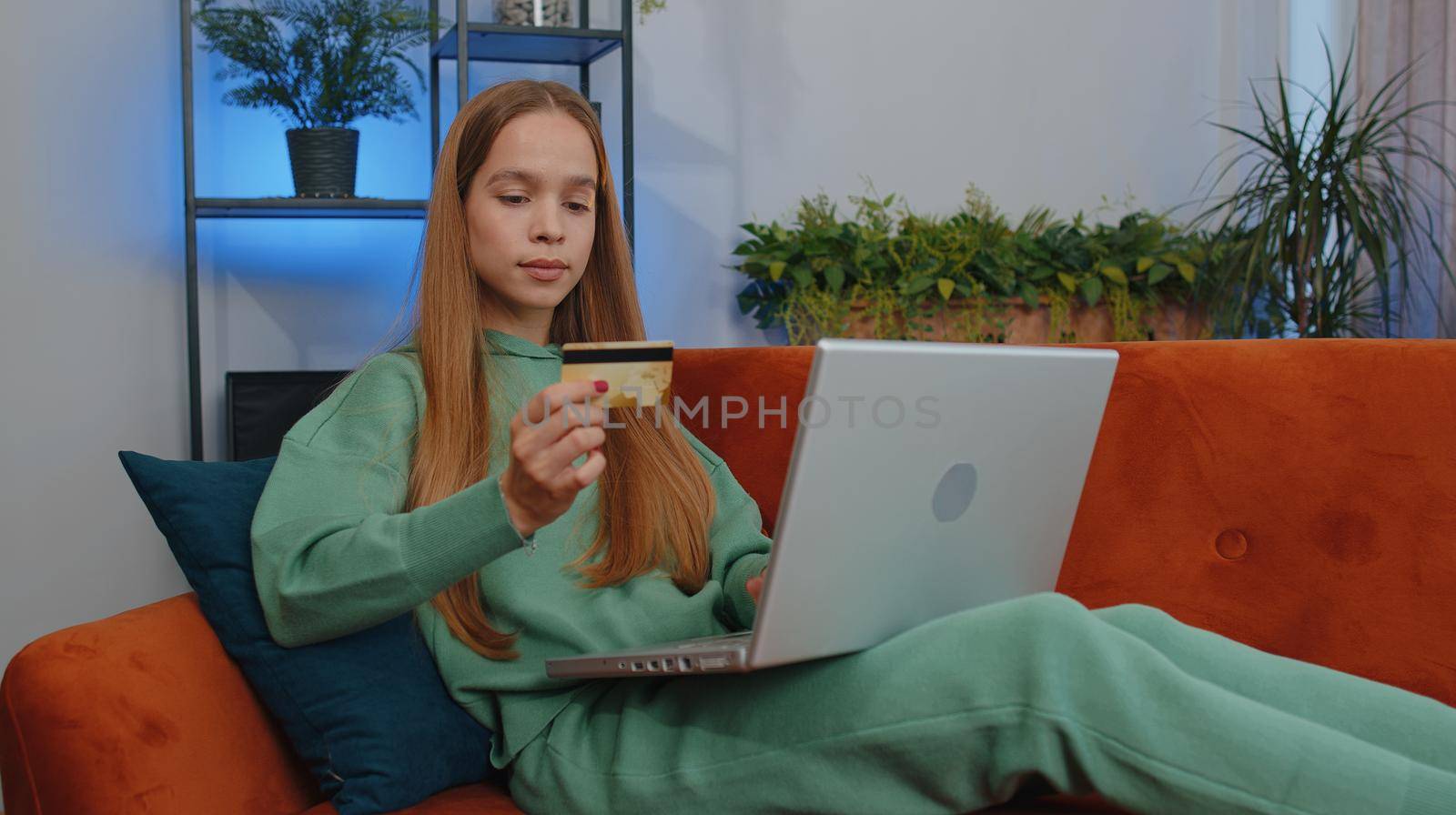Portrait of caucasian girl using credit bank card and laptop computer while transferring money, purchases online shopping, order food delivery at home. Young child kid sit on couch at home living room