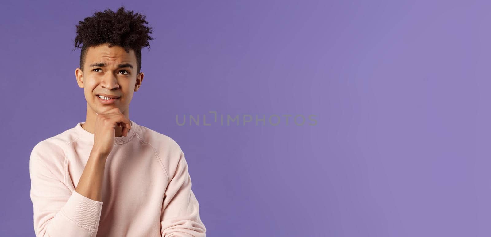 Close-up portrait of indecisive, puzzled young man facing difficult choice, look up thoughtful, touch chin and grimacing while thinking, making-up idea or decision, purple background.