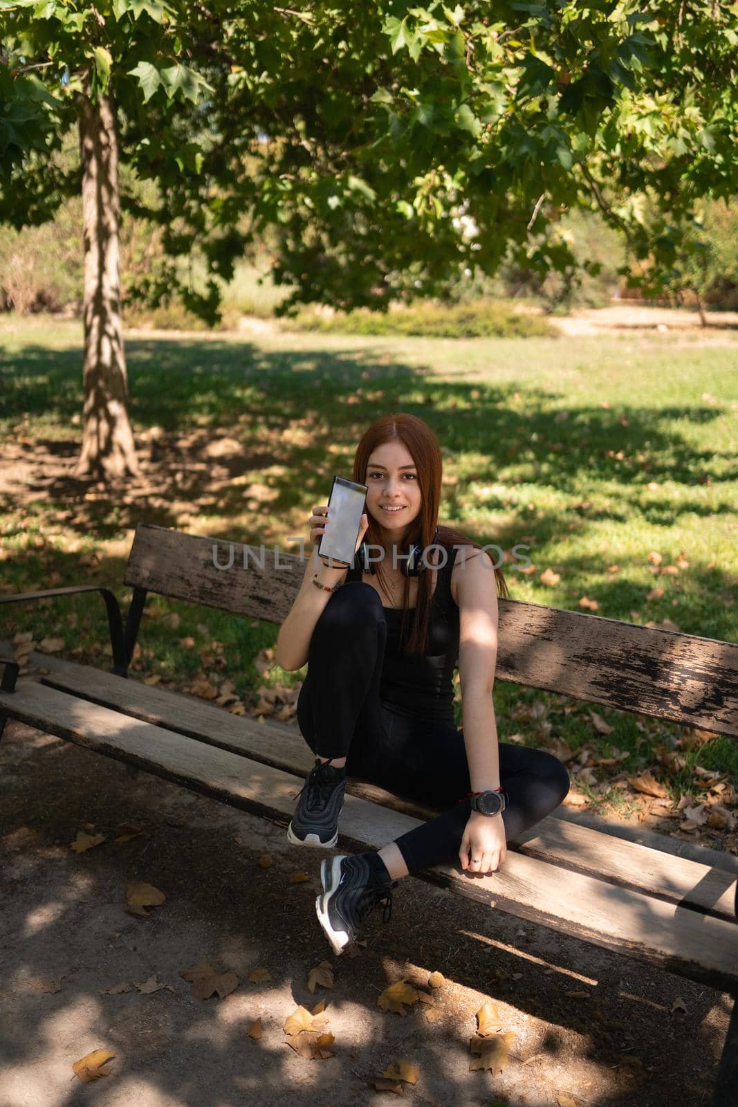 Smiling fit lady demonstrating phone on bench by barcielaphoto