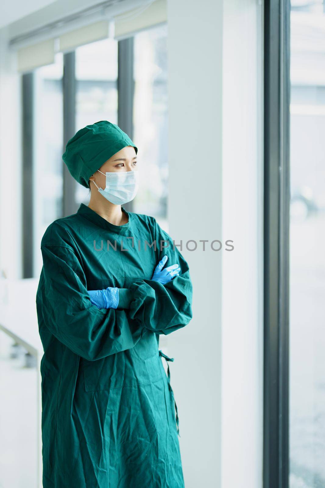 Portrait of an Asian doctor standing with his arms crossed by the window.