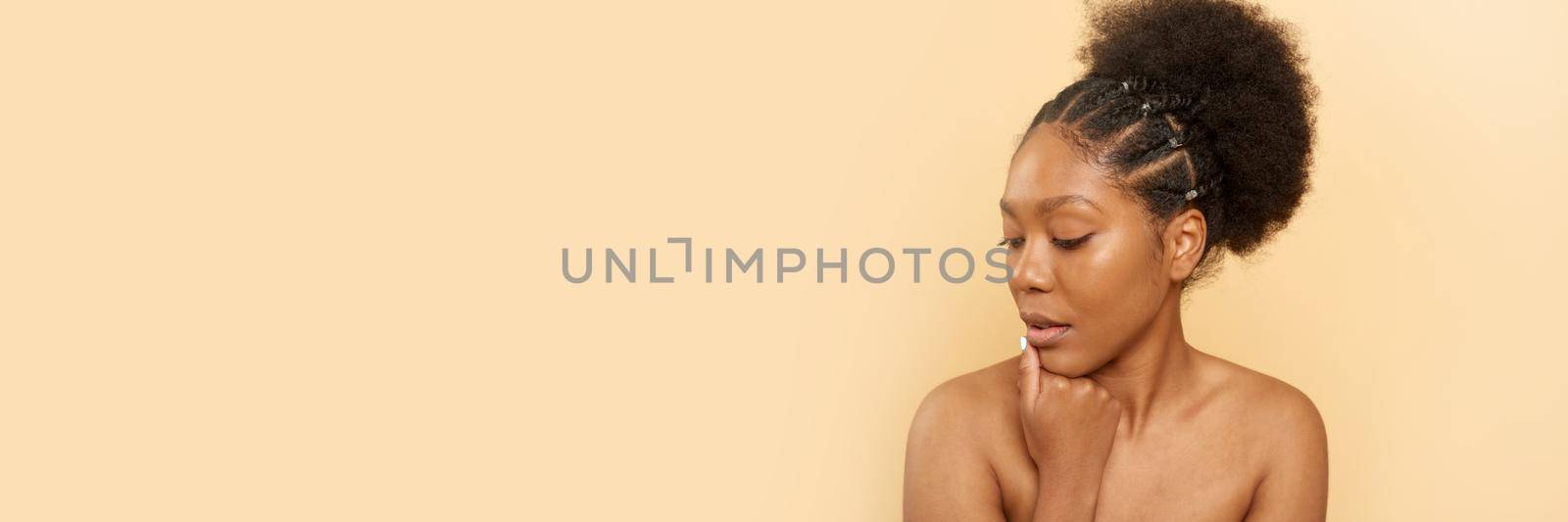 Positive young black woman with bare shoulders and beautiful skin on a beige background. Web banner.