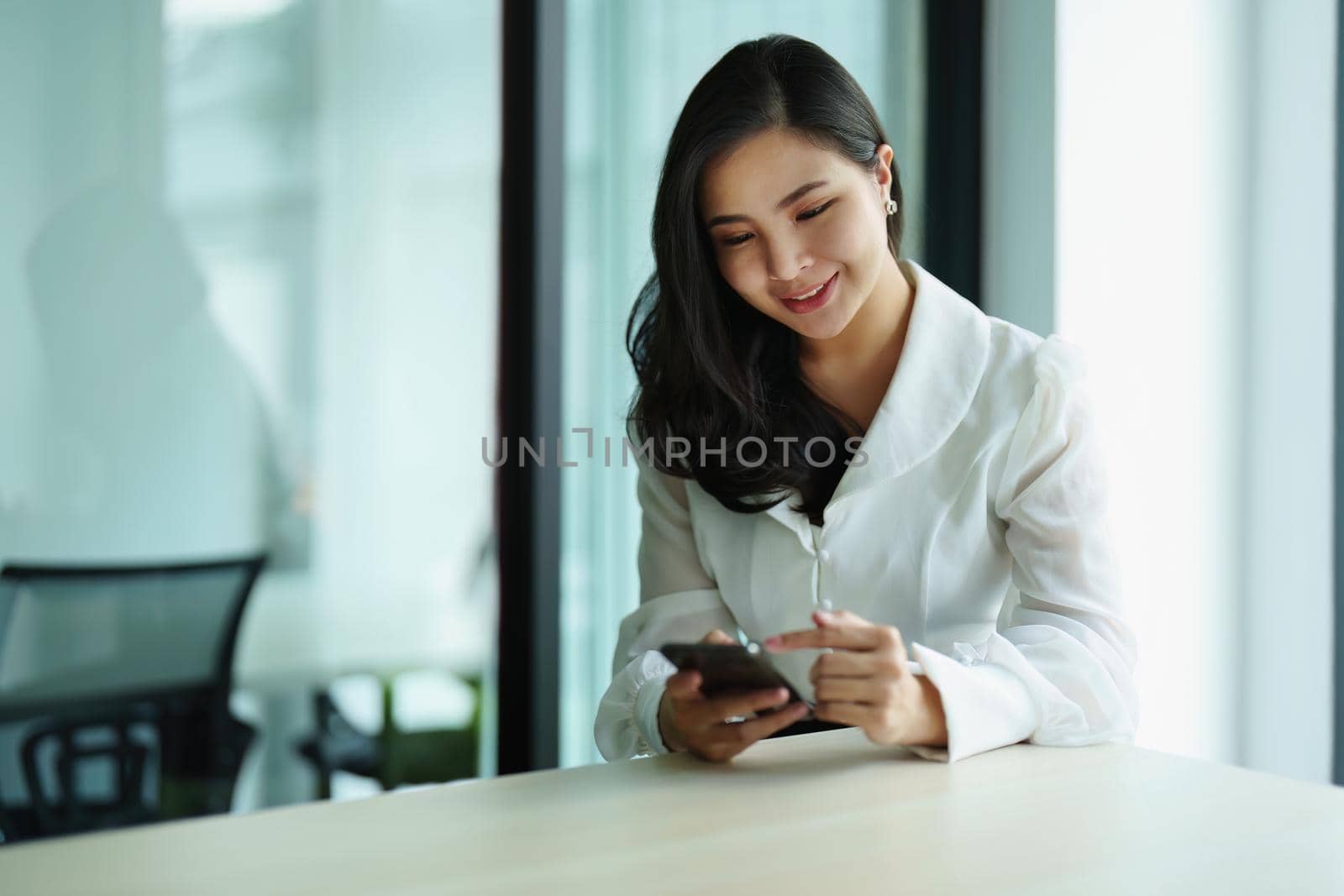 Portrait of a young Asian woman sitting at a desk using her phone.
