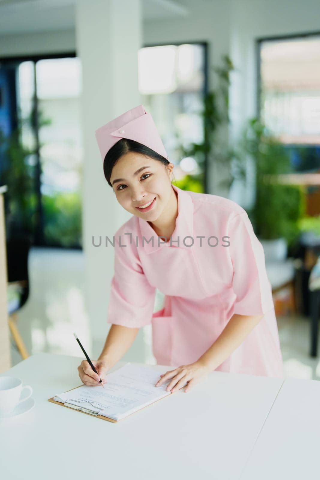 Portrait of a young Asian nurse looking at patient documents by Manastrong