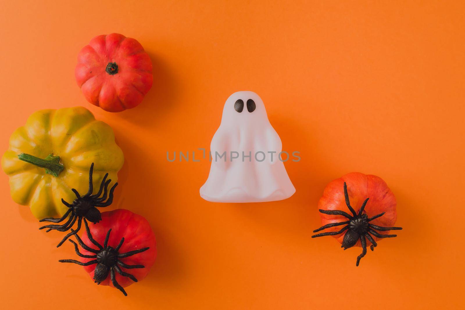 Cute ghost on a background of pumpkins and spiders on an orange background. Place for your text.