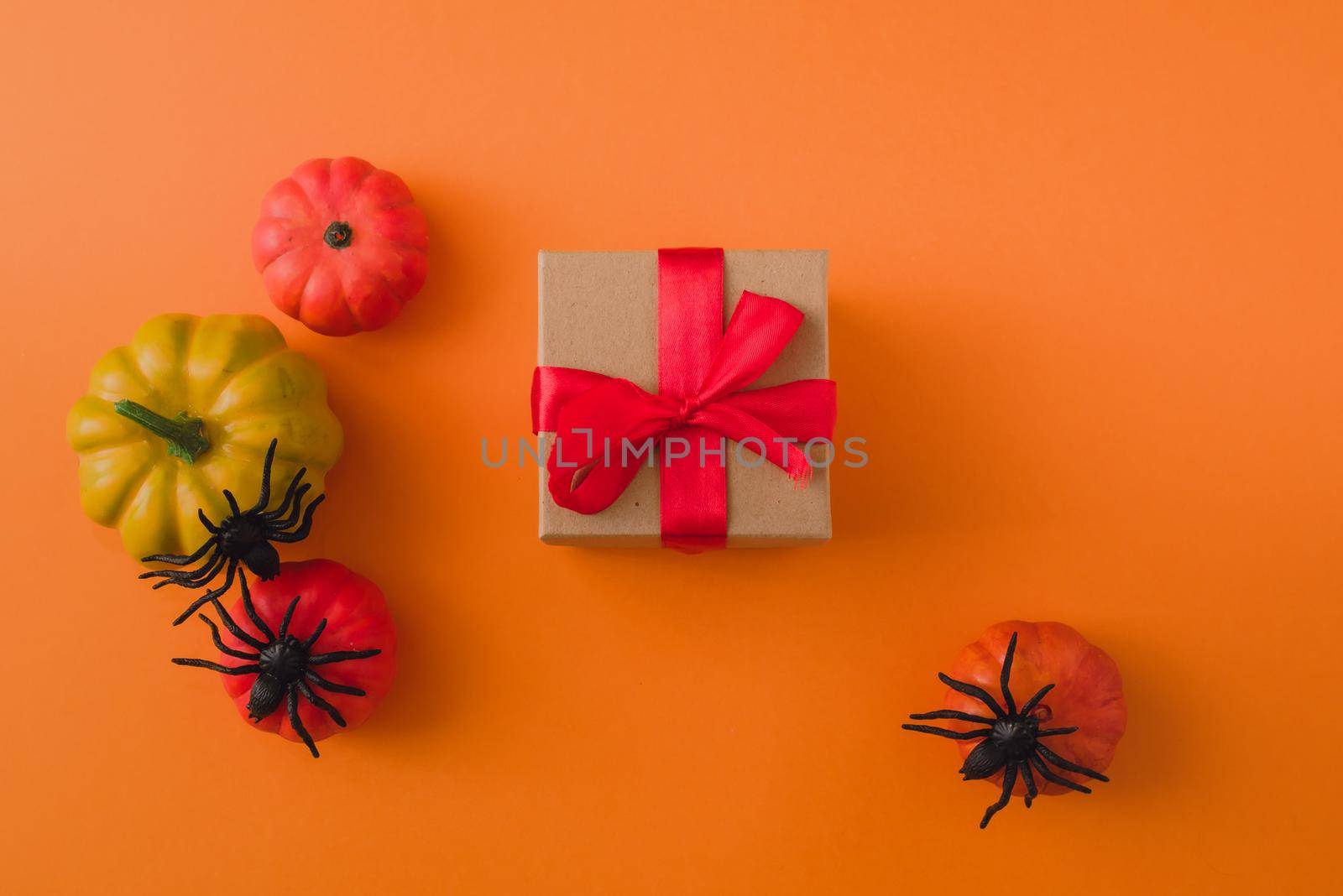 Gift on the background of pumpkins and spiders on an orange background. Place for your text.