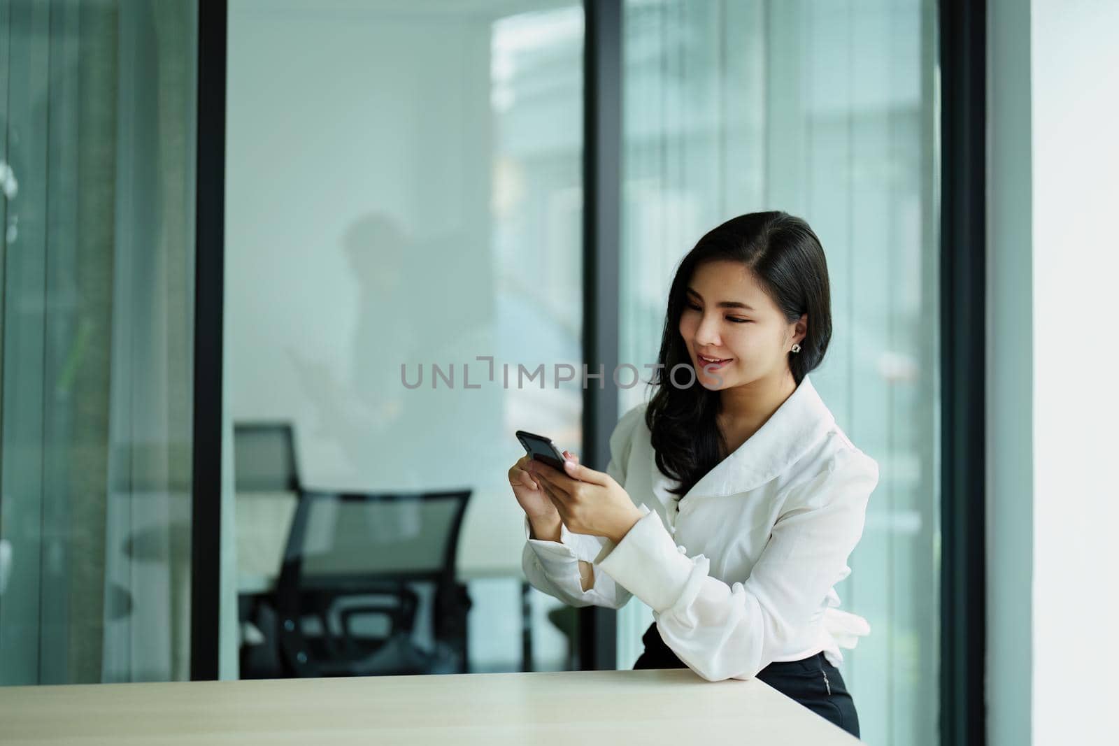 Portrait of a young Asian woman sitting at a desk using her phone.