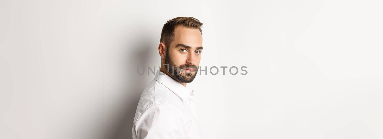 Close-up of professional business man turn face at camera, looking confident, standing against white background.