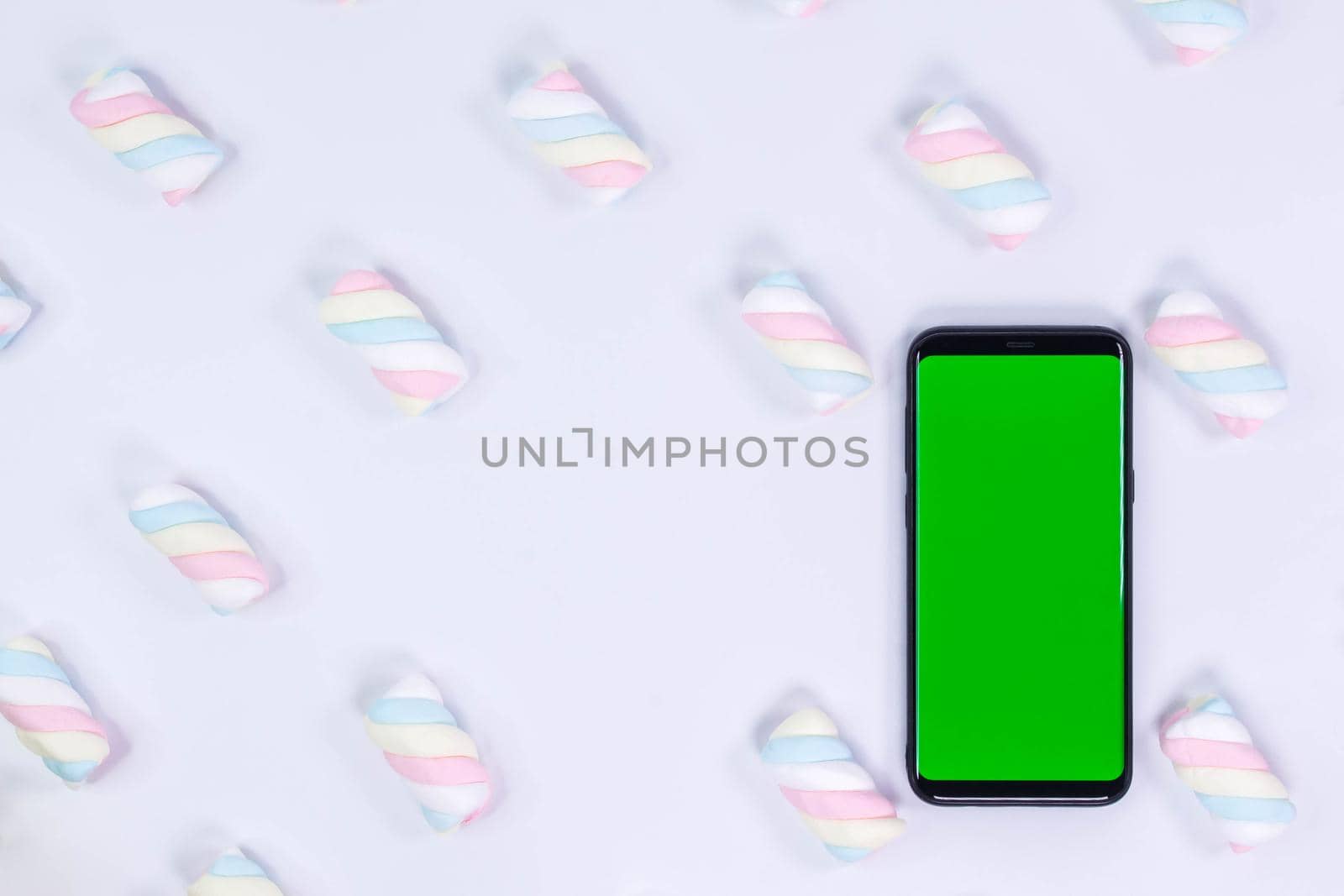 Phone mobile telephone with a vertical green screen. White background with twisted marshmallow pattern. Chroma key smartphone technology.