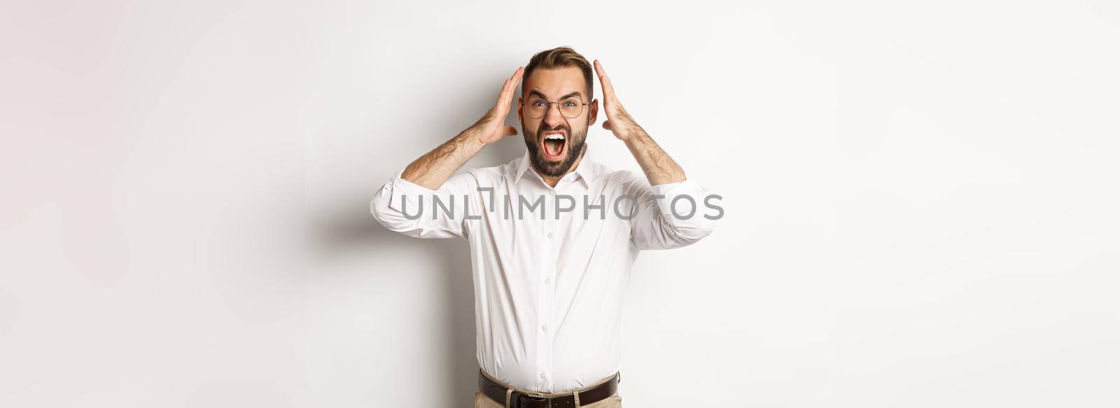 Frustrated man panicking, shouting and looking anxious, standing over white background.
