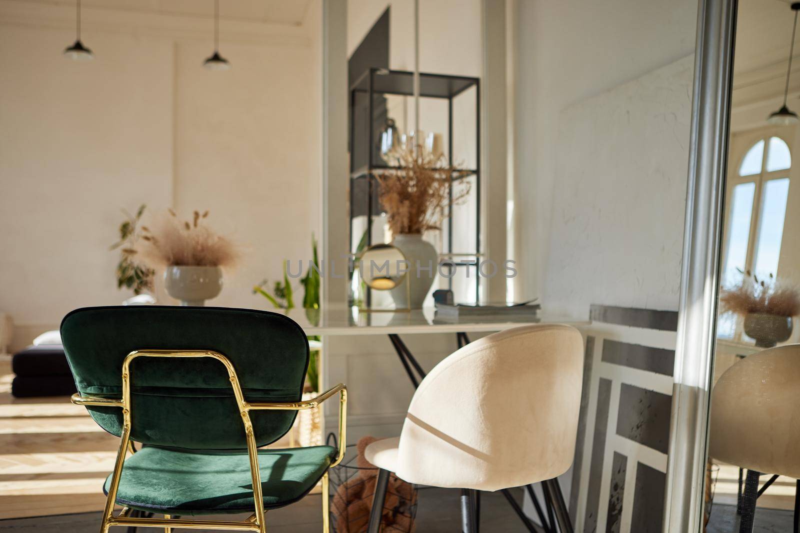 Soft velour green and beige armchairs at wall with mirror frame in bright sunlit room with flower vases