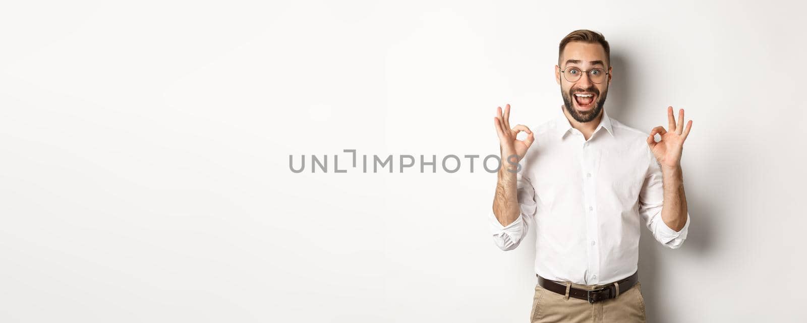 Amazed entrepreneur showing okay sign and looking happy, satisfied with product, standing over white background by Benzoix