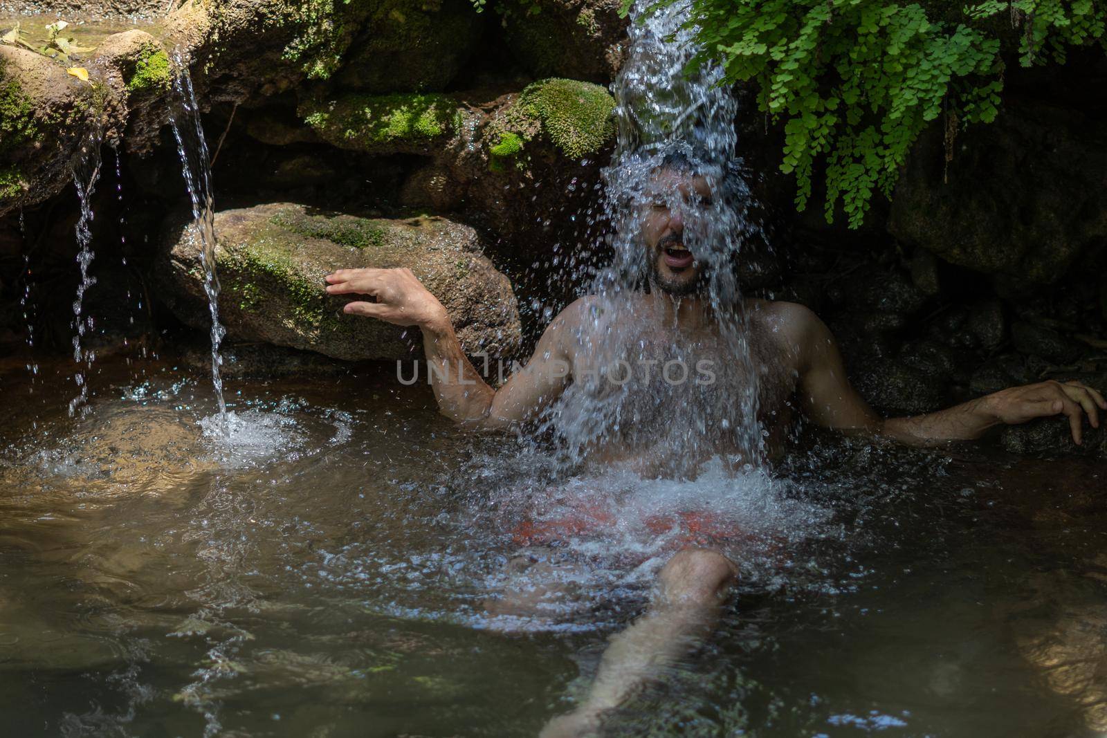 young man cooling off under a waterfall of cold, clear water