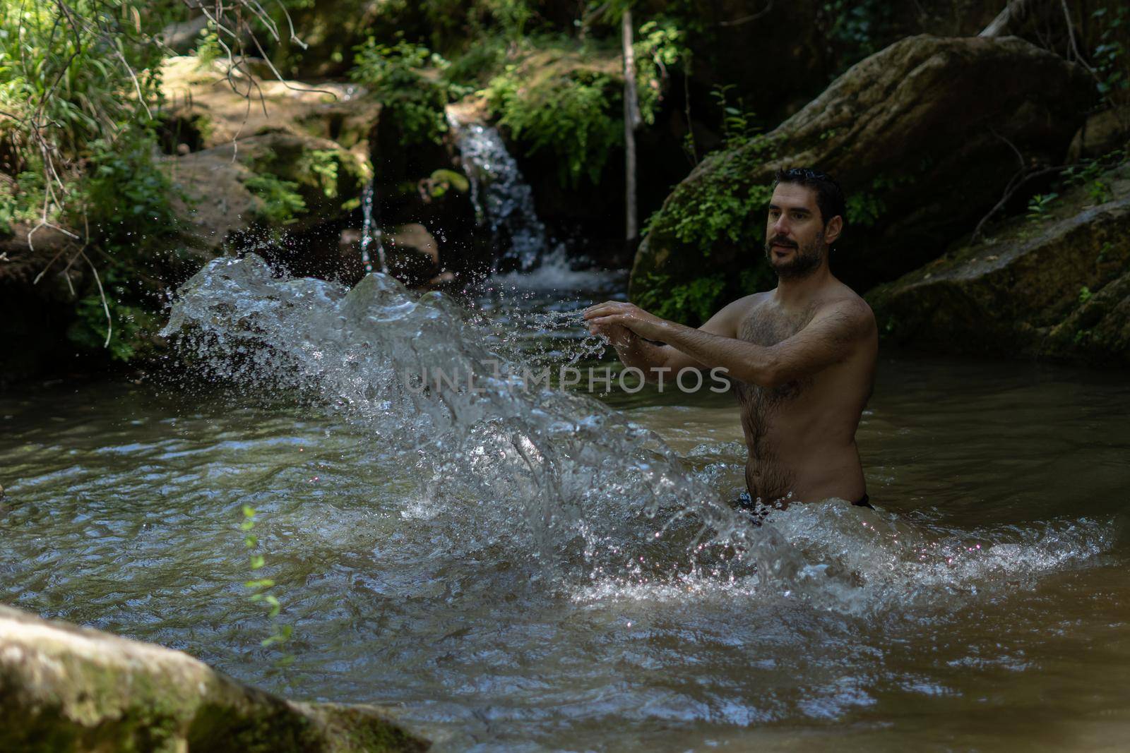young man in the river in swimsuit splashing water with his hands