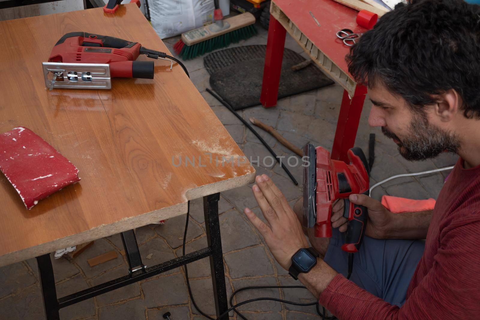 young man using carpenter's power tools making wooden furniture in his home