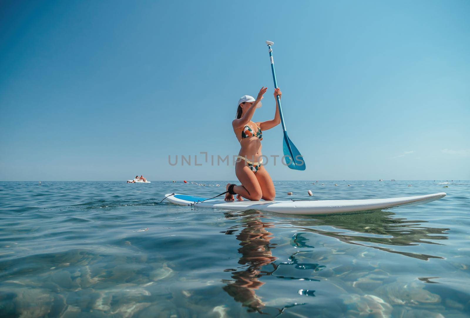 young woman in swimsuits doing yoga on sup board in calm sea, early morning. Balanced pose - concept of healthy life and natural balance between body and mental development