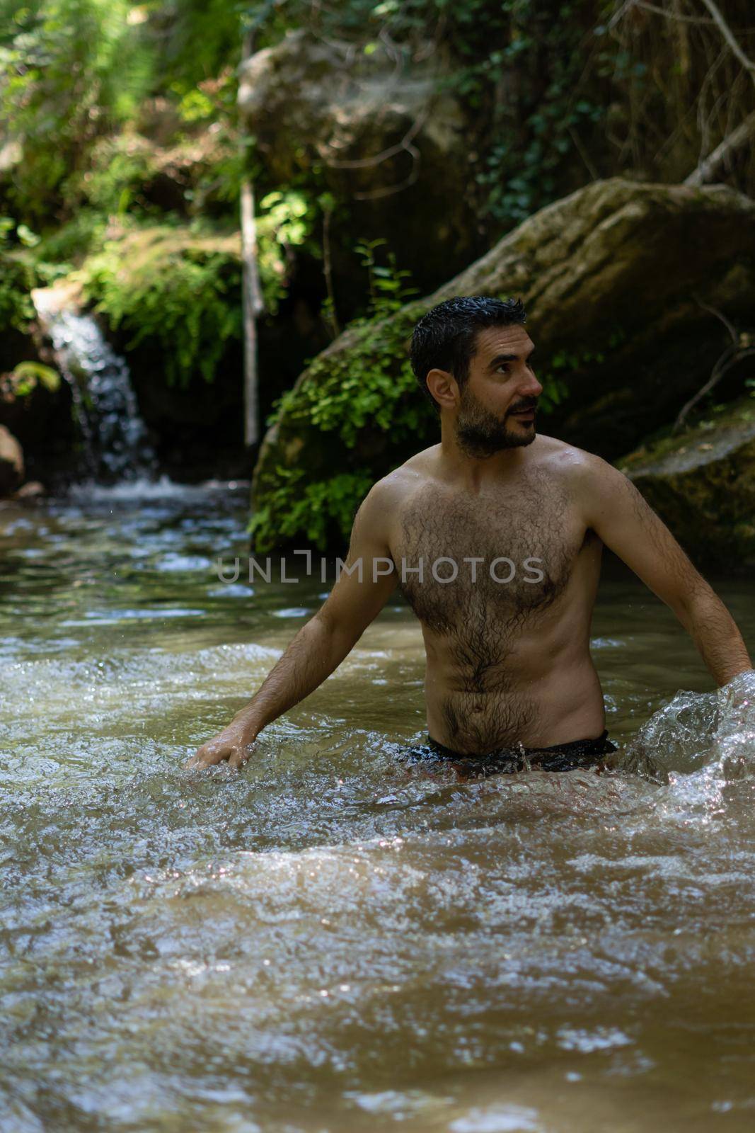 attractive young man bathing in a mountain river with a waterfall in the background