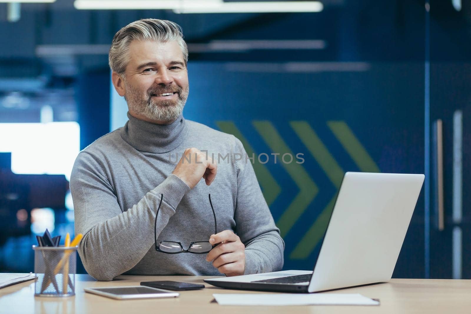 Portrait of senior gray-haired businessman, experienced mature man working with laptop inside office building, investor smiling and looking at camera