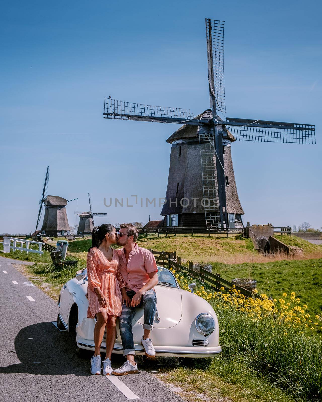 couple doing a road trip with an old vintage sports car by the Dutch windmill village Schermerhorn, a couple of men and women visiting the windmills in the Netherlands