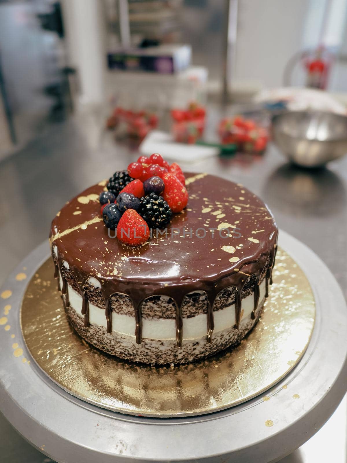hand of chef toppig a choco cake with gold and berries in the lab