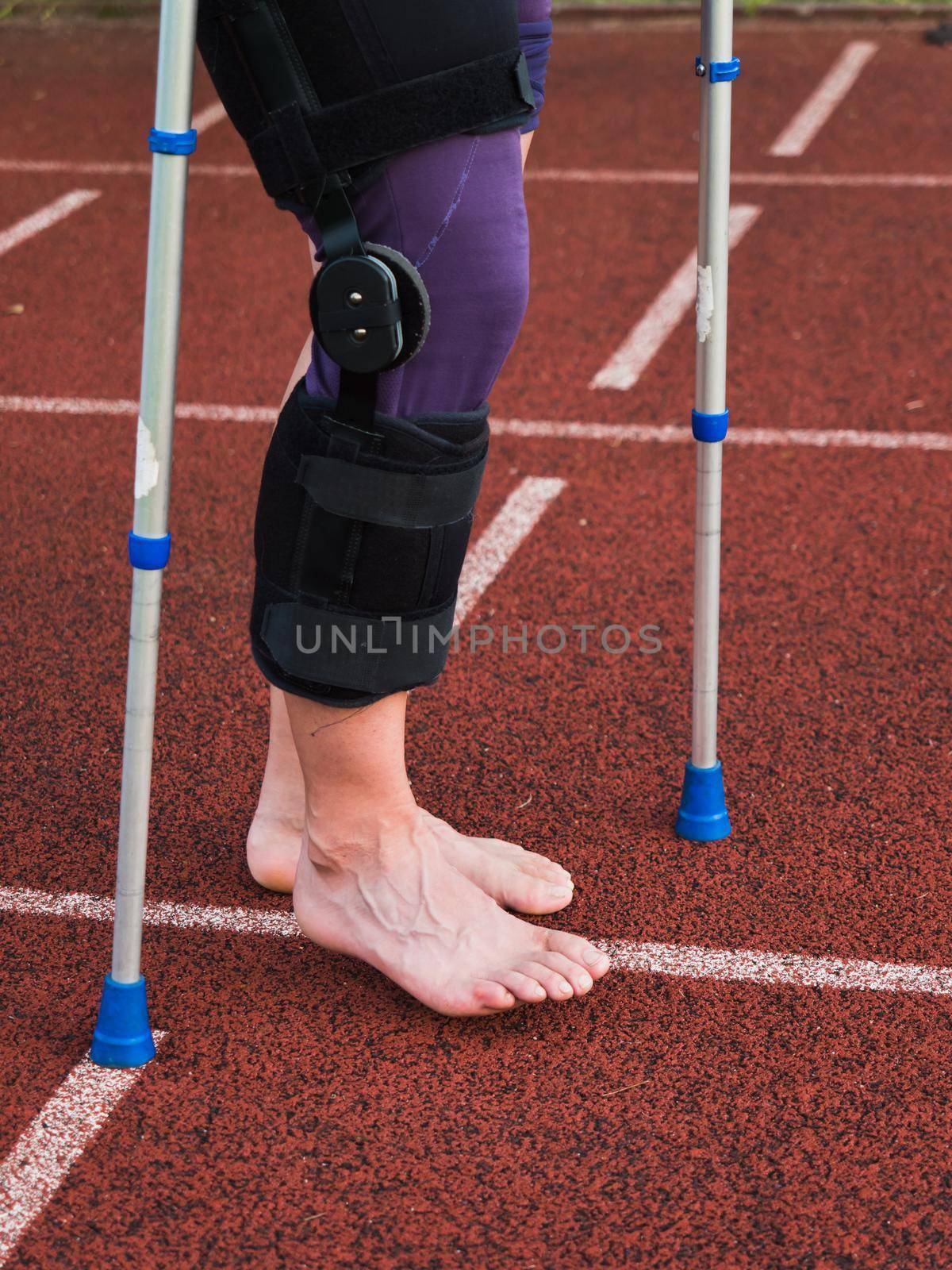 Hurt runner walk by forearm crutches on red running track after finished competition. The track of outdoor stadium