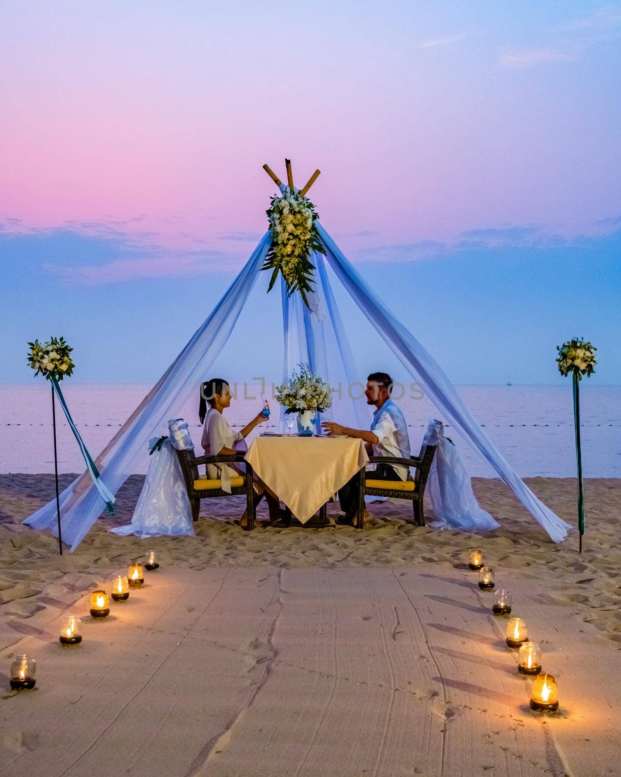 couple men and woman having romantic dinner with candle lights on the beach in Thailand by fokkebok