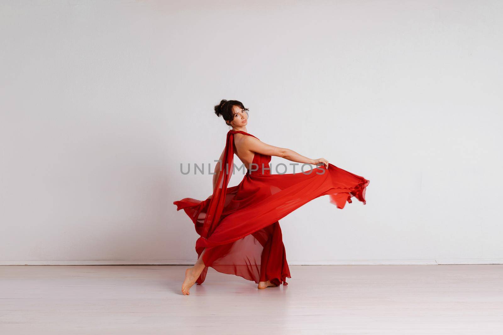 Dancer in a red flying dress. Woman ballerina dancing on a white studio background.
