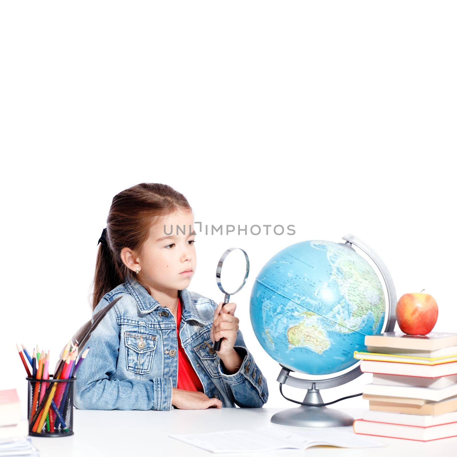 Curious little girl looking through magnifying glass on globe by Taut