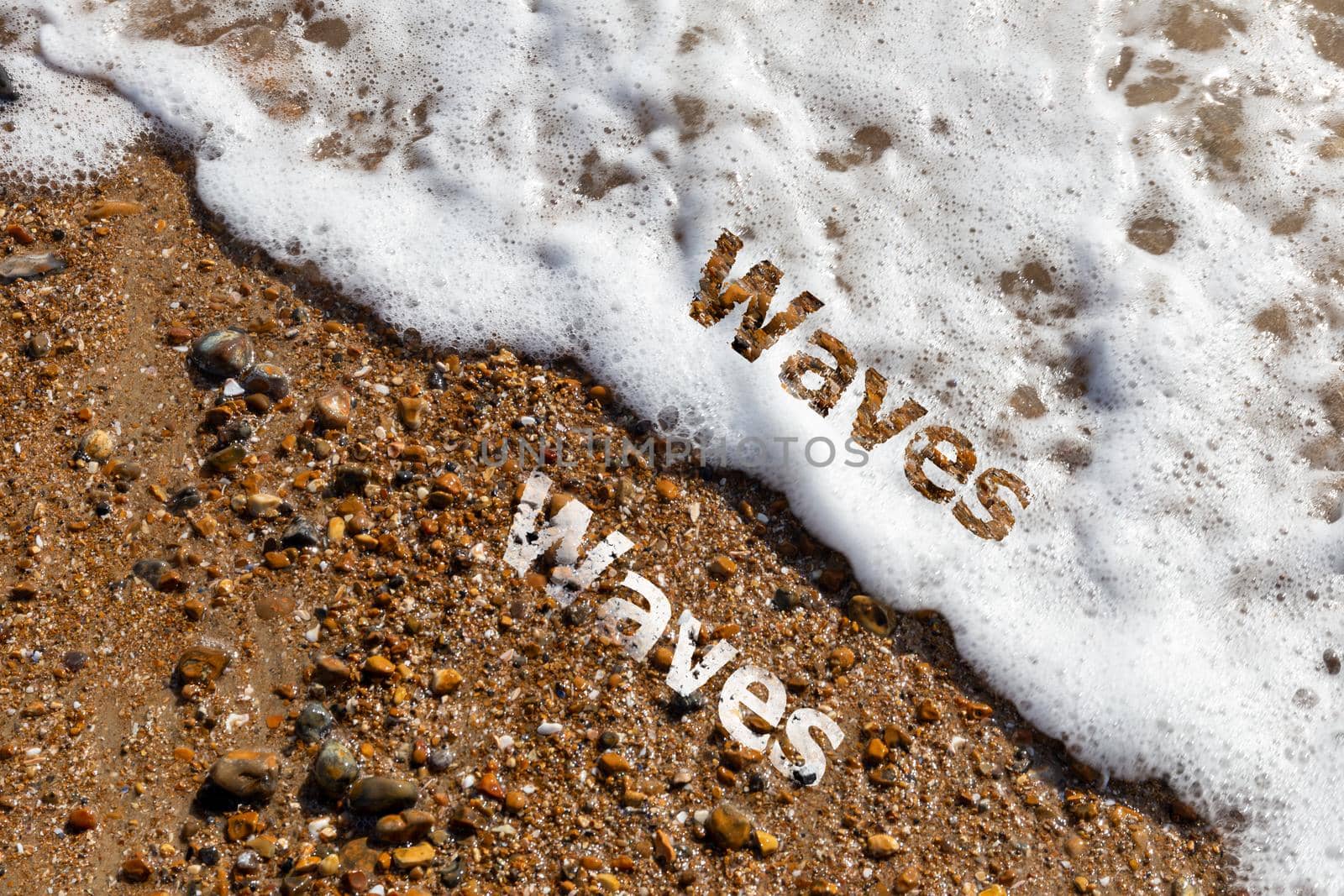 Waves text cut out on both pebble beach and lapping waves