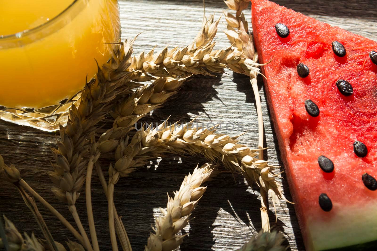 Freshly squeezed orange juice, sweet watermelon dessert and spikelets of ripe wheat on a wooden table in the sunlight...