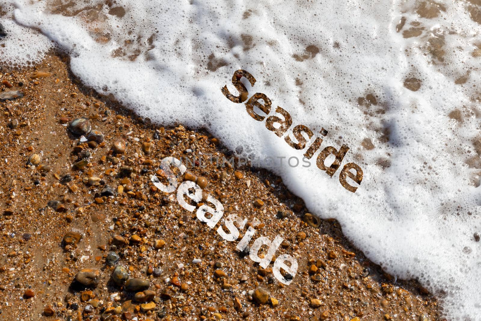 Seaside text cut out on pebble beach and lapping waves by magicbones