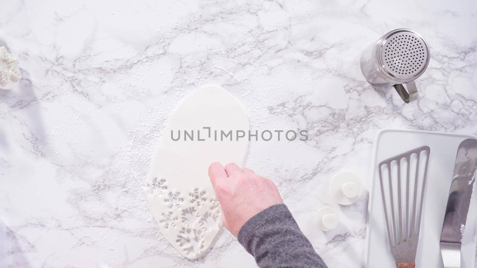 Flat lay. Step by step. Cutting out snowflakes with cookie cutters out of white fondant on a marble counter.