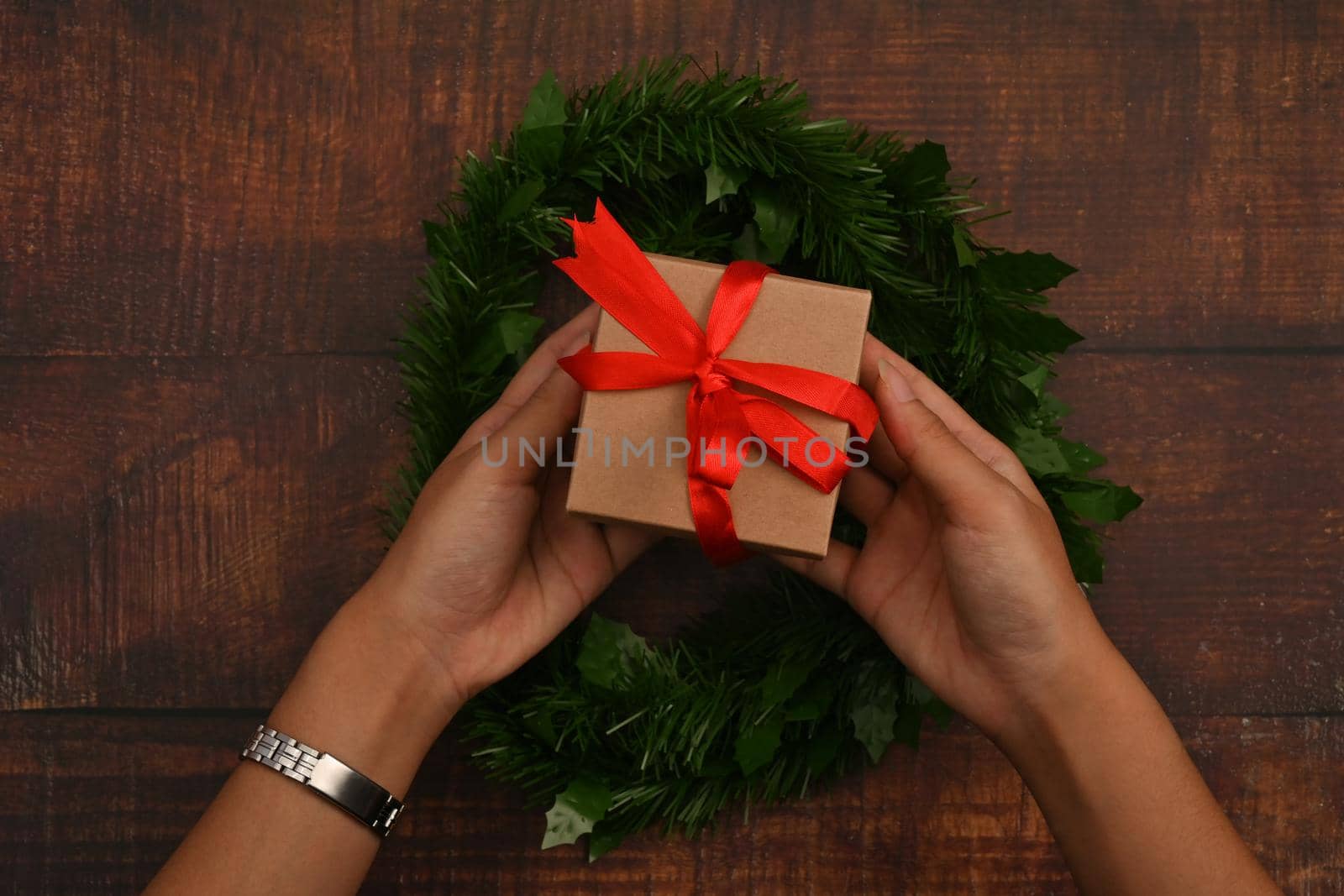 Overhead view of woman hands holding Christmas Gift on wooden background. New year and Christmas concept.