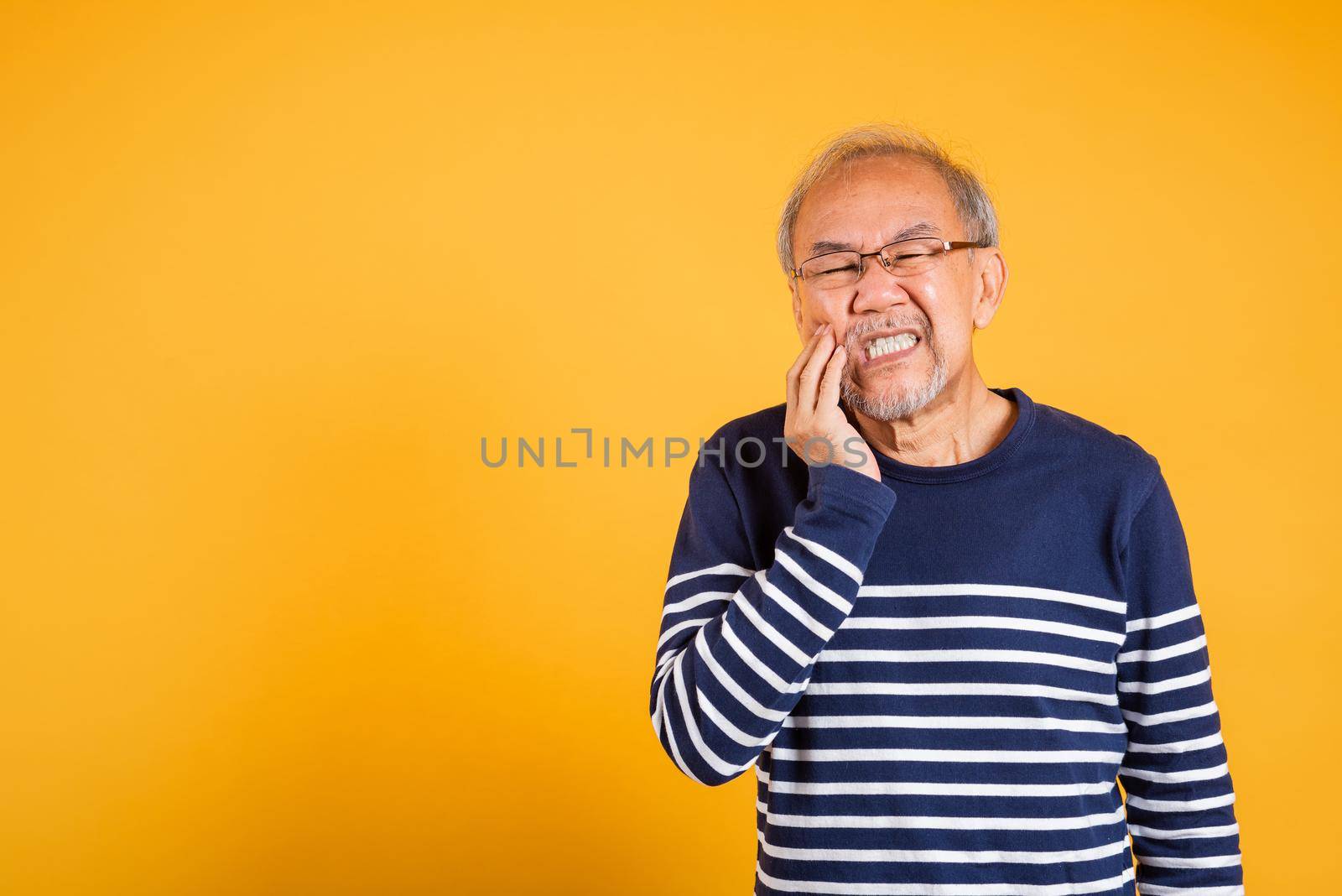 Dental pain. Portrait senior old man sad hand touching cheek suffering from toothache studio shot isolated on yellow background, Asian unhappy elder man problems with teeth pain, dental healthcare