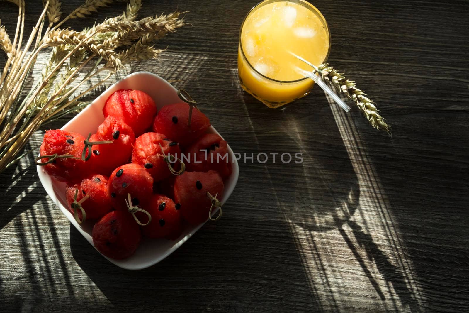 Freshly squeezed orange juice, sweet watermelon dessert and spikelets of ripe wheat on a wooden table in the sunlight...