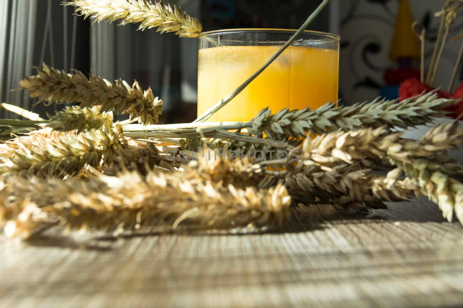Freshly squeezed yellow juice and spikelets of ripe wheat on a wooden table in the sunlight.,,