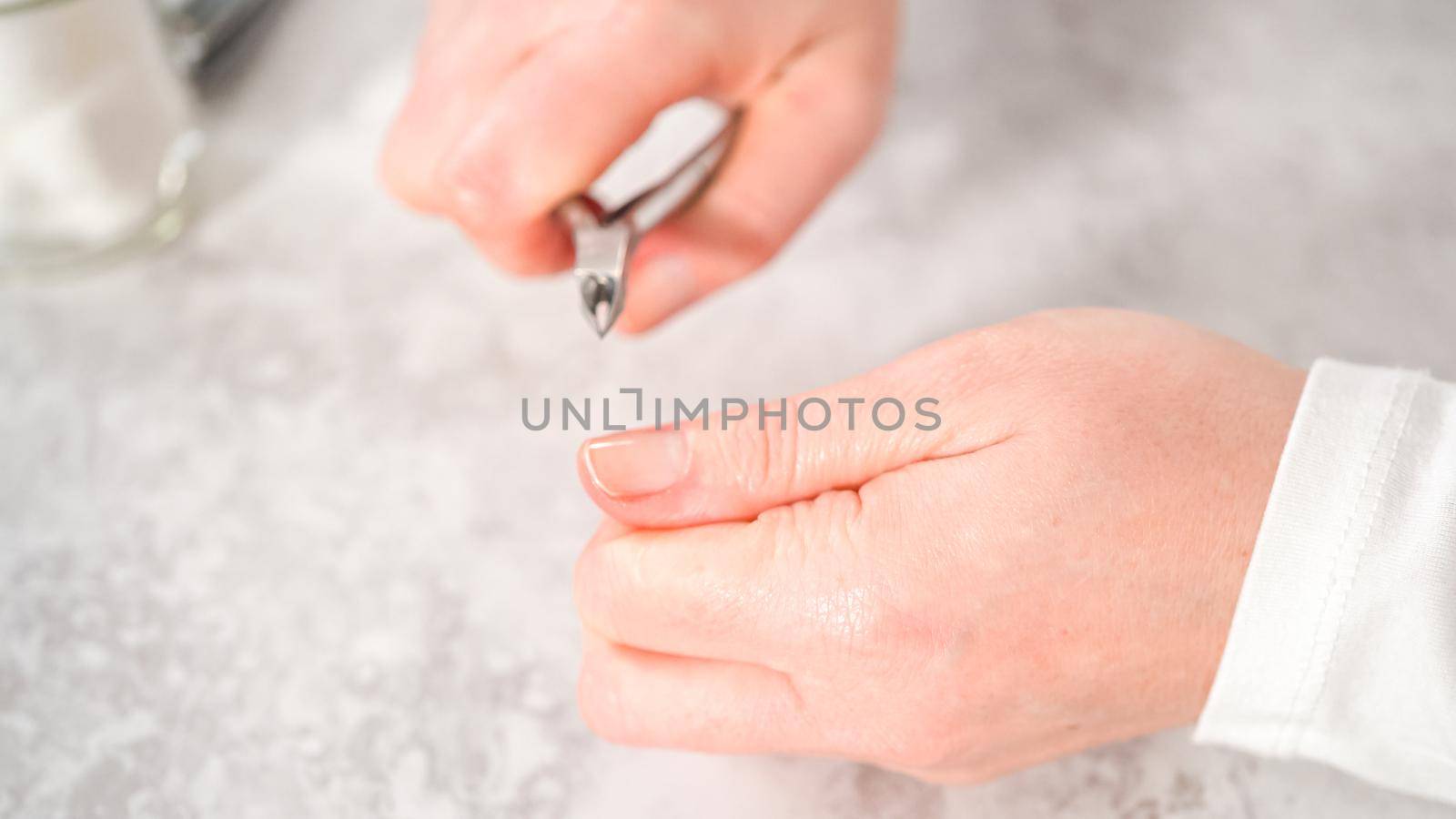 Woman finishing her manicure at home with simple manicure tools. Cutting out cuticles around the nails.