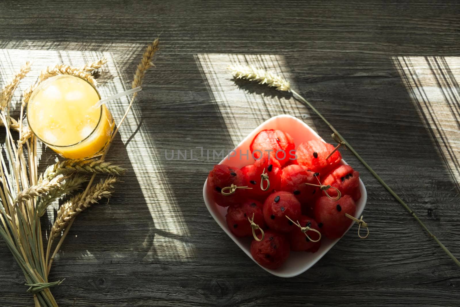 Freshly squeezed orange juice, sweet watermelon dessert and spikelets of ripe wheat on a wooden table in the sunlight...