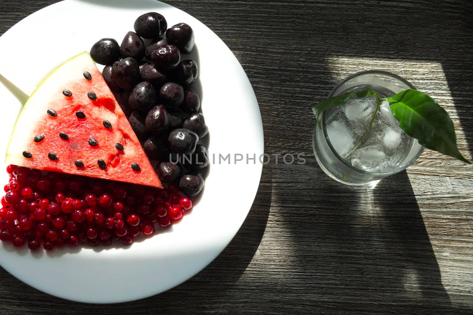 Summer snack. Fresh berries and fruits on a wooden table with green leaves of plants.
