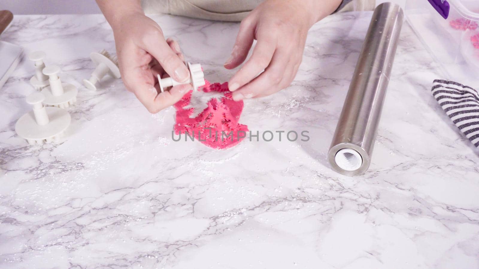 Step by step. Cutting out snowflakes with cookie cutters out of pink fondant on a marble counter.